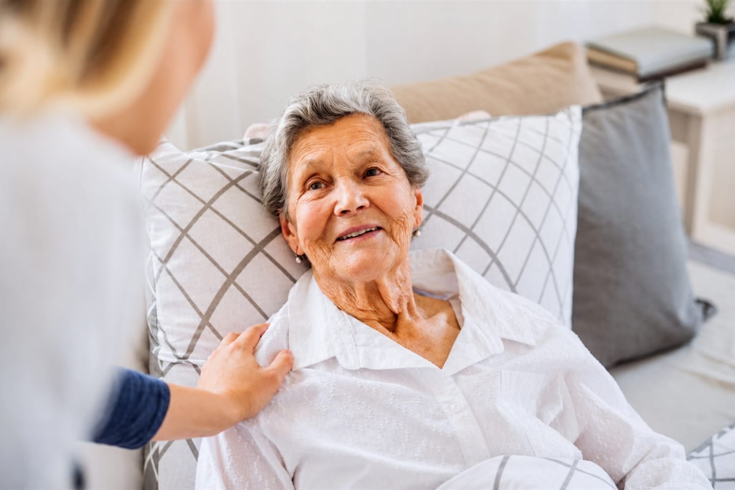 A care provider resting a hand on the shoulder of a patient resting in bed